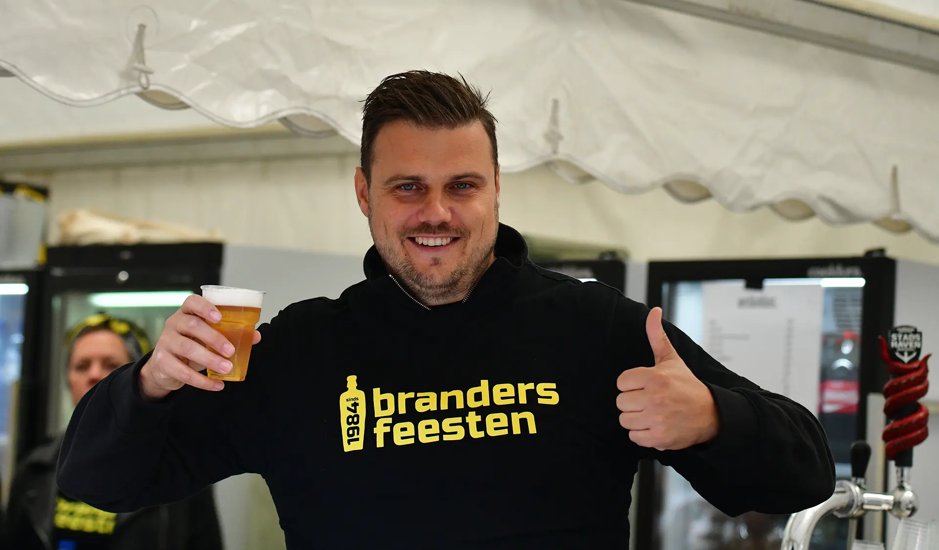Een medewerker van de Brandersfeesten houdt een drankje vast en steekt zijn duim op